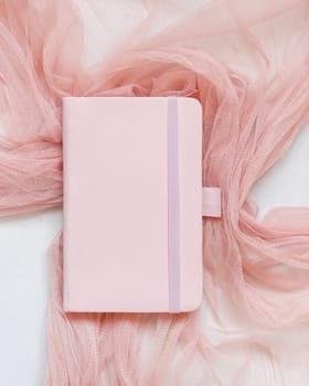 Pink hardcover notebook on tulle fabric on white table top view. Romantic mockup. Educational and Back to school concept