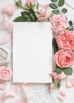 Blank card near light pink roses, engagement ring in a box and silk ribbons on white table top view, wedding mockup. Romantic flat lay with Vertical card and pastel decor