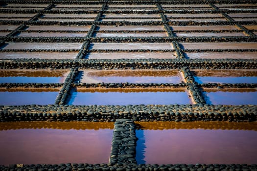 View on traditional rectangular salt evaporation ponds or salt pans creating a grid showing different stages of evaporation and concentration.