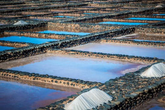 View on traditional rectangular salt evaporation ponds or salt pans creating a grid showing different stages of evaporation and concentration.