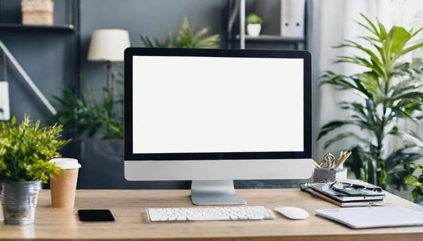 Modern personal computer with blank white screen, keyboard, mobile phone and office accessories on desk at workplace of graphic designer, blogger. Electronic devices, technology and creativity