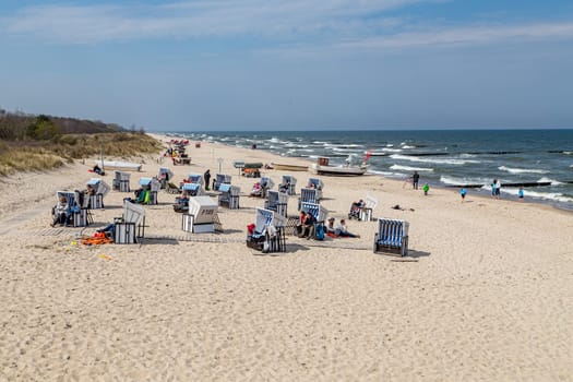 Koserow, Germany - April 20, 2014: people enjoy the sun in the roofed wicker beach chair, the typical beach couches at the baltic sea in Usedom, Germany.