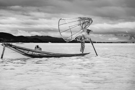 Heho, Myanmar - AUG 15, 2015 : Intha fisherman fishing  in his typical canoe with fishing net. The fishing net is handmade by the fisher.
