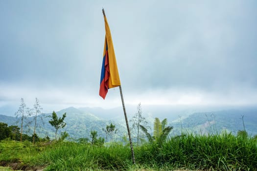 Misty and fogy landscape with colombian flag on high peak. Trek to hidden ancient ruins of Ciudad Perdida in Colombian jungle. Santa Marta, Sierra Nevada mountains, Colombia wilderness.