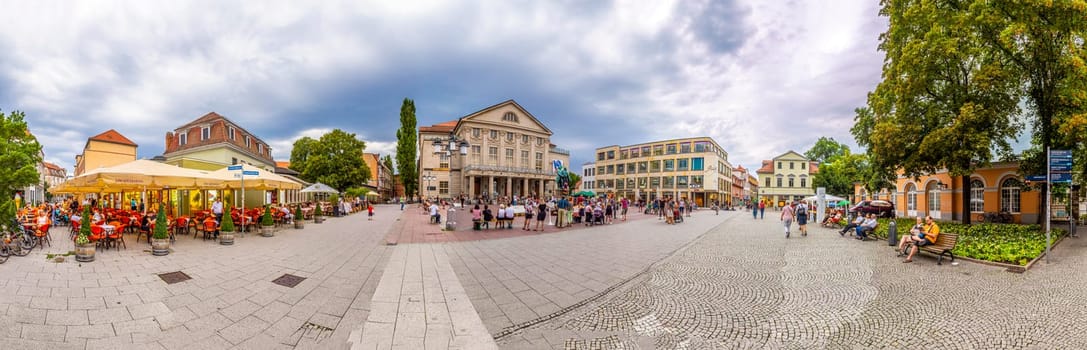 Weimar, Germany - July 28, 2018: people enjoy walking around the old town of Weimar with statue of Goethe and SChiller and facade of historic theater on a summer day.