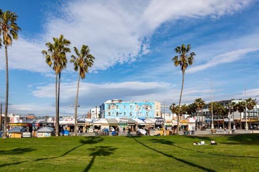 Venice, USA - March 5, 2019: people enjoy scenic beach promenade with palms and colorful houses at Venice Beach in California.