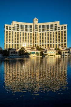 Las Vegas, USA - May 25, 2022: people pose at scenic historic famous Las Vegas welcome sign. view to Bellagio hotel with reflection in the lake in early morning light, Las Vegas, USA.