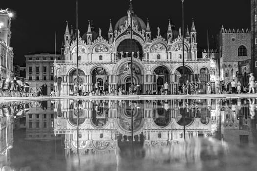 Venice, Italy - July 7, 2021: tourists at the square St. Marco by night with reflection of famous st. Marks cathedral.