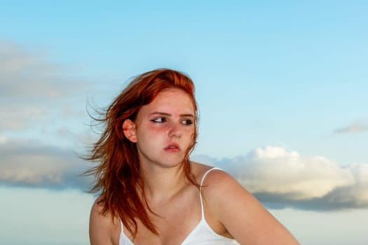 Young girl with red hair, on the beach in summer, her hair tousled by the wind