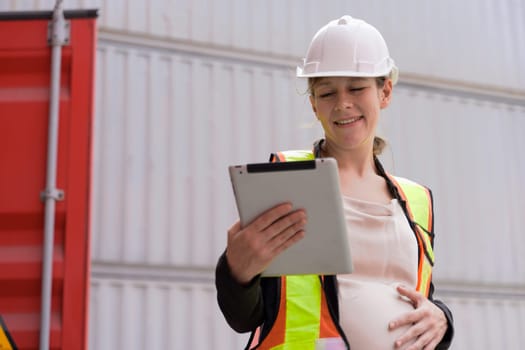 Portrait of smiling female pregnant using digital tablet and manging import and export containers while standing in cargo shipping yard