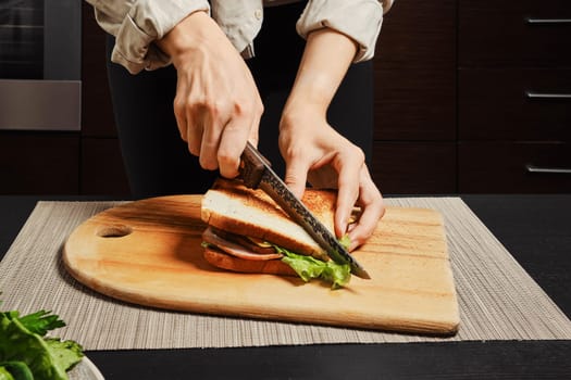 Unrecognizable woman cuts on half homemade club sandwich