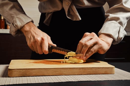 Unrecognizable woman slicing peeled ginger root into thin strips