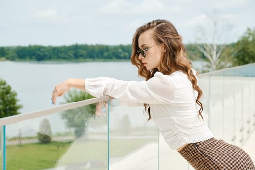 Young woman with long curly hair enjoying beautiful view from balcony