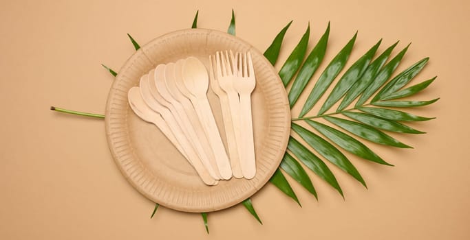 Paper plates, wooden spoons and forks on a beige background, top view