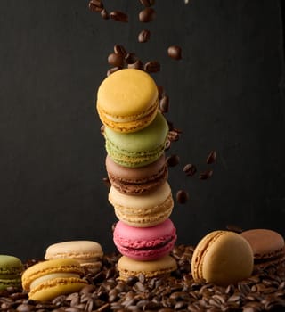 Stack of colorful macarons and flying coffee beans on a black background