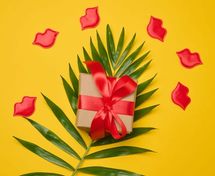 Gift box with red satin ribbon and bow on a yellow background. Holiday background