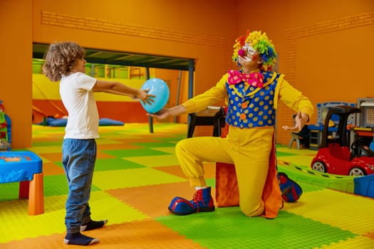 Funny playful games with clown at indoor playroom for children. Happy boy child and artist enjoying creative show with balloons at birthday party. Holiday celebration for kids concept
