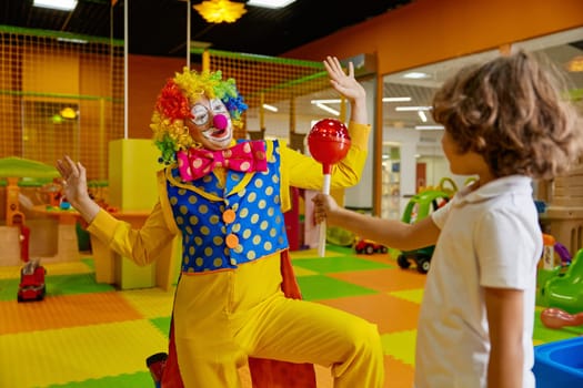 Birthday celebration at kids playroom with animation program concept. Little boy giving huge lollypop candy for surprised clown