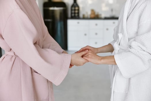 Closeup girl friends wearing bathrobe holding hands each other sharing support and help. Concept of trust, compassion empathy or forgiveness