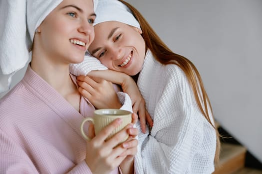 Young two girl friends or sisters wearing bathrobe hugging enjoying morning time together. Friendship and sisterhood, good relationships and bonding concept