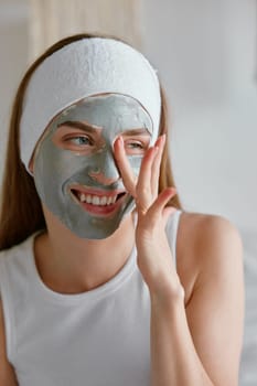 Young woman applying clay facial cosmetology mask on her face with hand. Healthy skin and beauty, home spa procedure with natural cosmetics concept