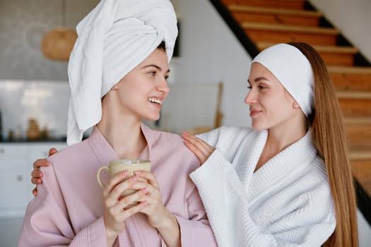 Young two girl friends or sisters wearing bathrobe hugging enjoying morning time together. Friendship and sisterhood, good relationships and bonding concept