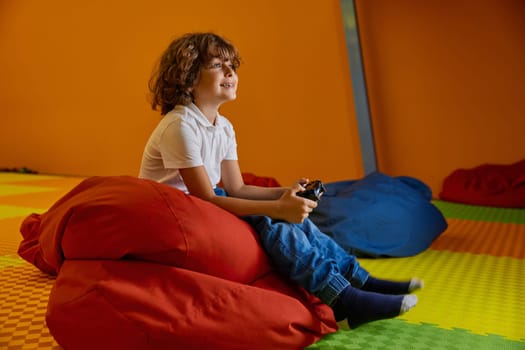 Portrait of cute little boy child holding joystick playing computer video game at kids center while having fun on weekends
