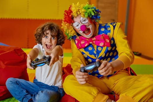 Portrait of little boy child and funny clown playing video games together. Happy kid and artist with happy faces and humorous grimace expressing joyfulness and cheerful emotion