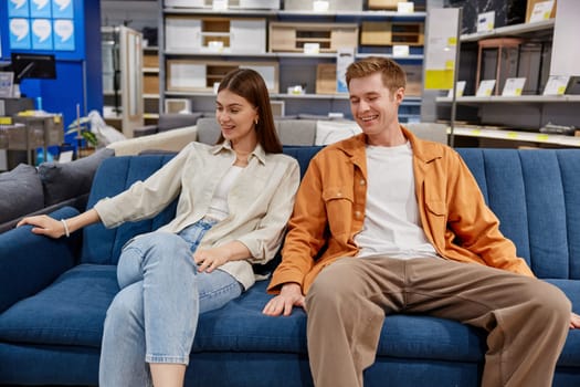 Relaxed man and woman couple sitting on sofa testing comfort of furniture. Shopping at furnishing showroom