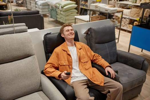 Relaxed man sitting at comfortable leather armchair feeling peace and no stress enjoying shopping time at modern furniture retail market