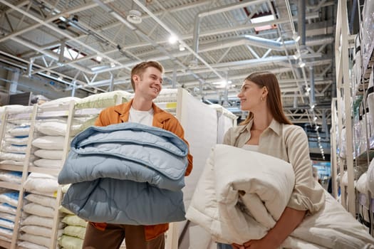 Happy young couple choosing new bedding blanket for home at linen store. Man and woman feeling satisfaction of shopping with sales buying two item for price of one