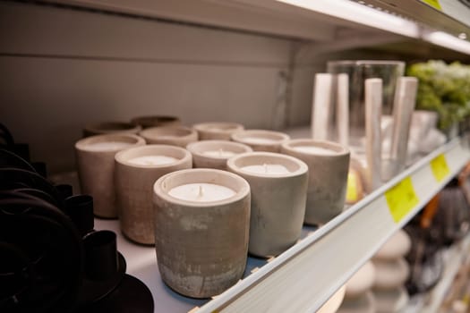 Scented aroma candles in plaster candlestick at promotional price standing on rack at household store. Handmade craft decorative item for home design inferior