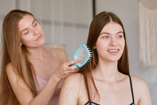 Young woman brushing hair of her female friend headshot portrait. Friendship and femininity concept