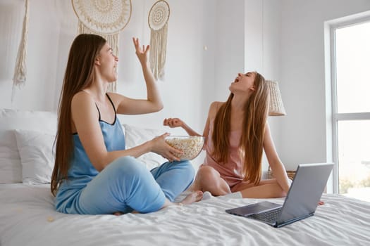 Relaxed young girl friends with popcorn enjoying film watching entertainment. Sleepover, bonding and night for cinema streaming concept