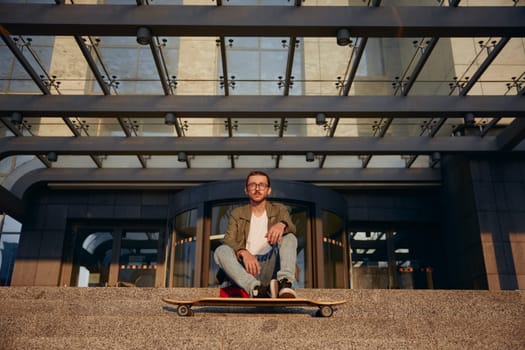 Cool guy student with longboard rest on stairs of university urban building. Skateboard as means of city transportation