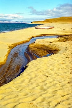 The sandy shore of Baikal, a boat on the shore and a streamlet. Autumnal nature on Lake Baikal. Landscape and flora of Baikal