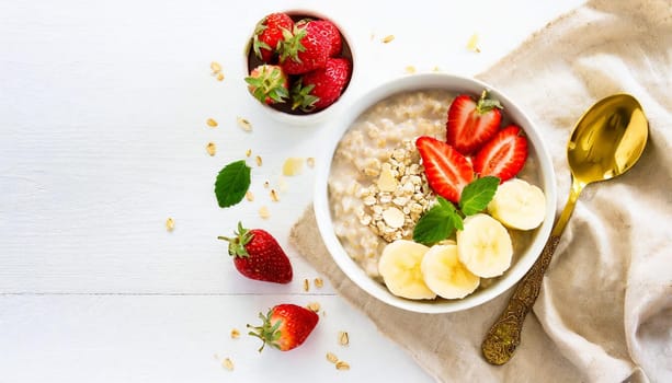 Bowl of oatmeal porridge with strawberry and banana on white table top view. Healthy and diet breakfast.