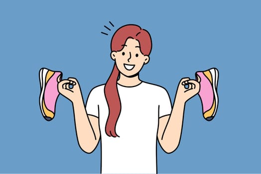 Teenage girl holds running shoes for running or fitness training, recommending use high-quality shoes for sports. Positive woman with beauties in hands invites you to joint workout in gym or marathon