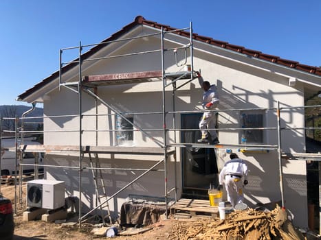 Fischbach, Germany - March 8, 2022: New construction site with finished base plaster, worker at scaffold.