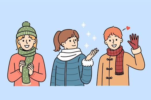 Little kids in winter clothes stand under falling snow, rejoicing at onset of christmas weekend at school. Cheerful boys and girls waving hands and catching snowflakes during christmas holidays