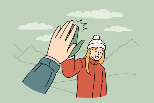 Woman tourist gives five to friend hiking in mountains to explore new picturesque places. Girl in warm jacket and hat enjoys hiking, which allows to improve health and take mind off work.
