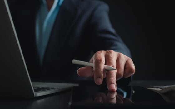 Businessman in black suit working on laptop computer and tablet, Hand Hands touch on tablet at office with dark background, Online working, Close up, Copy space.