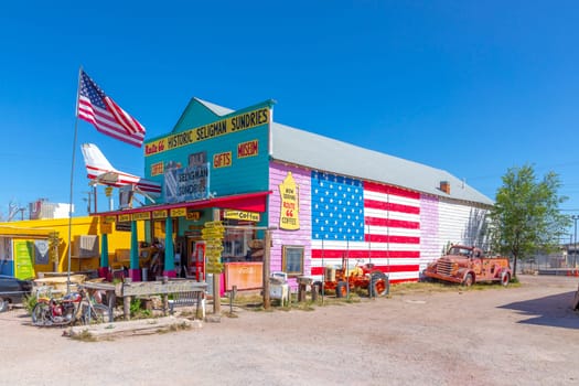 Seligman, USA - May 25, 2022: colorful facade of Shop Historic Seligman Sundries with stars and stripes and an aircraft crashed in the facade and vintage car at route 66 in Seligman, USA.