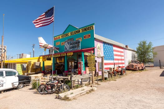 Seligman, USA - May 25, 2022: colorful facade of Shop Historic Seligman Sundries with stars and stripes and an aircraft crashed in the facade and vintage car at route 66 in Seligman, USA.