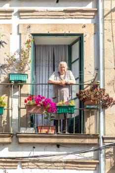 Braga, Portugal - May 1, 2023: elderly lady watches the street from her balcony in the old town of Braga, Portugal.