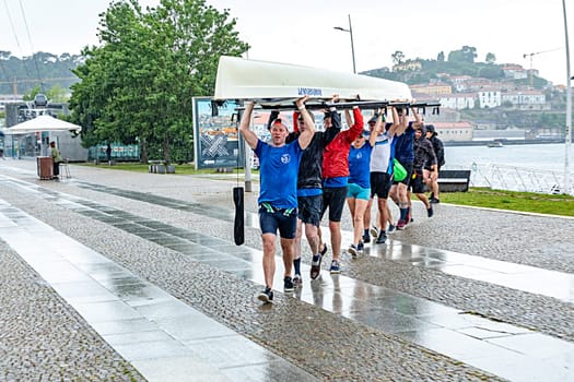 Porto, Portugal - May 3, 2023: rowers in  team of eight carry the rowboat to the rowboat hall in heavy rain in Porto.