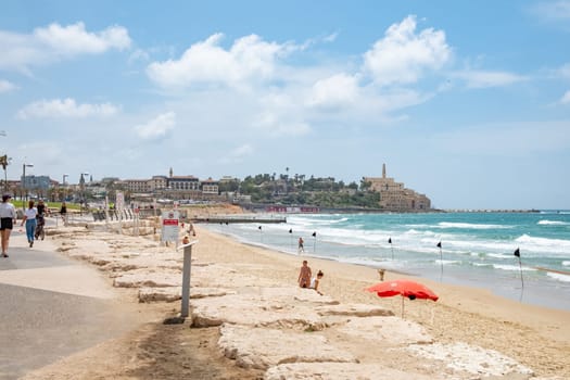Tel Aviv, Israel - May 18, 2023: people enjoy the beautiful sandy beach in Tel Aviv on a summer day. In the background the old town of Tel Aviv.