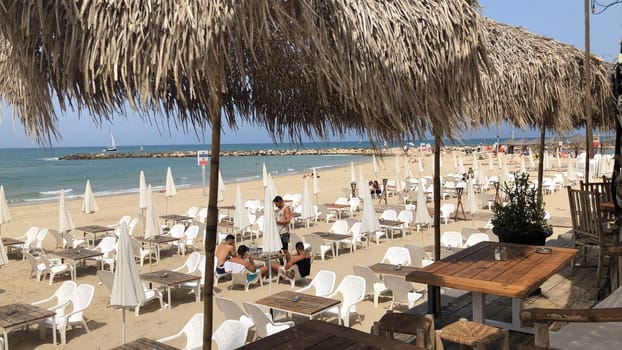 Tel Aviv, Israel - May 21, 2023: people enjoy the beach in Tel Aviv and sit under bamboo parasols and relax at beach couches in the midday heat.