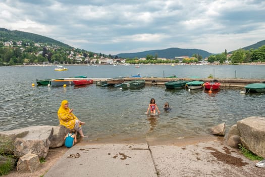 Geraldmer, France - June 18, 2023: muslim family enjoys swimming in the gerldmer lake with boats and beautiful landscape in background.