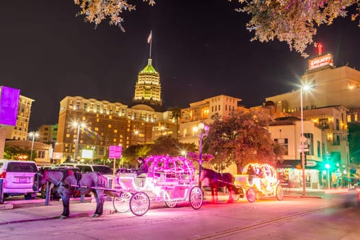 San Antonio, USA - October 31, 2023:  people enjoy to have a ride by night in the horse drawn carriage with colorful neon light in San Antonio at the river walk area.
